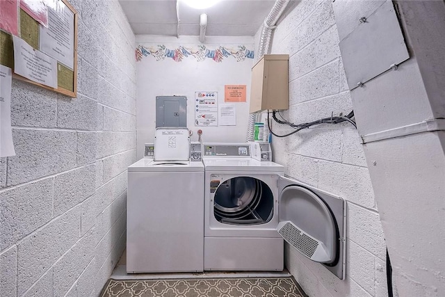 shared laundry area featuring concrete block wall, electric panel, and independent washer and dryer