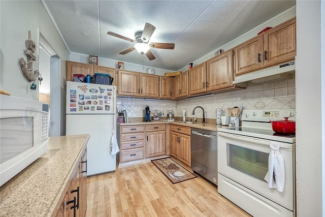 kitchen with light countertops, a sink, light wood-type flooring, white appliances, and under cabinet range hood