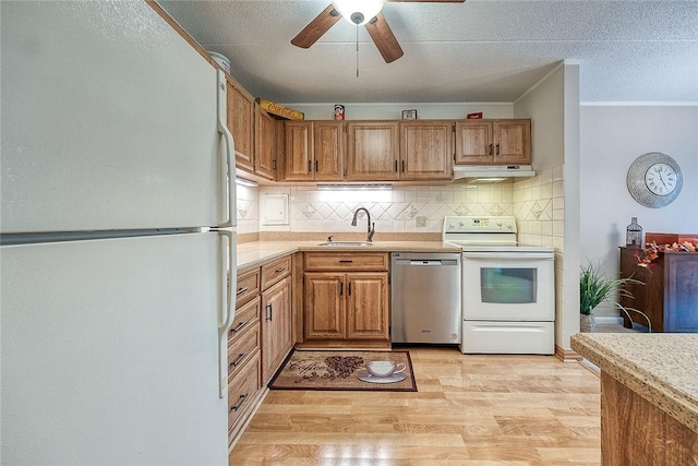 kitchen with tasteful backsplash, light countertops, a sink, white appliances, and under cabinet range hood