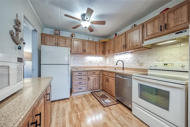 kitchen with white appliances, light countertops, light wood-type flooring, under cabinet range hood, and a sink