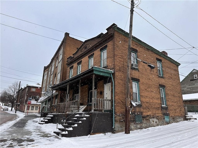 view of snowy exterior featuring cooling unit, covered porch, brick siding, and central AC unit