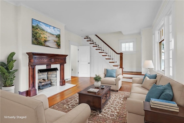 living area featuring stairs, a fireplace, ornamental molding, and wood finished floors