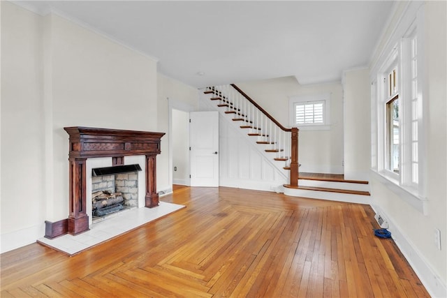 unfurnished living room with a fireplace with raised hearth, baseboards, ornamental molding, stairway, and hardwood / wood-style floors