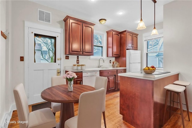 kitchen with a breakfast bar, visible vents, a sink, light wood-type flooring, and white appliances