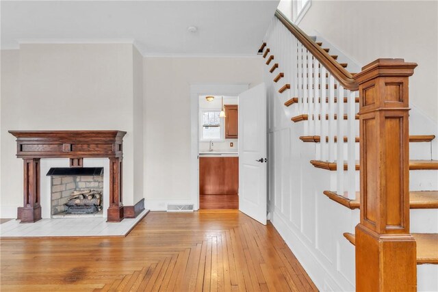 unfurnished living room featuring a fireplace, visible vents, stairs, light wood-type flooring, and crown molding