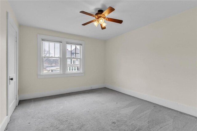 carpeted spare room with a ceiling fan and baseboards