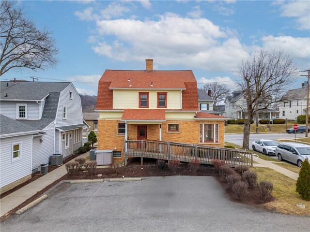 view of front facade with brick siding, a chimney, uncovered parking, central AC, and a residential view