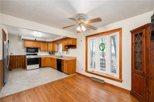 kitchen featuring light wood finished floors, light countertops, brown cabinetry, a sink, and black appliances