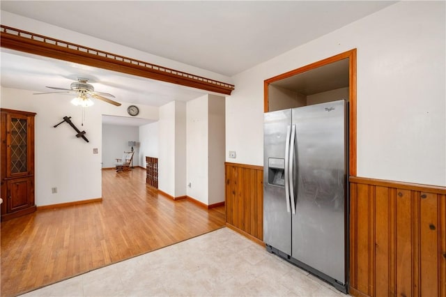 kitchen with ceiling fan, wood walls, light wood-style floors, wainscoting, and stainless steel refrigerator with ice dispenser