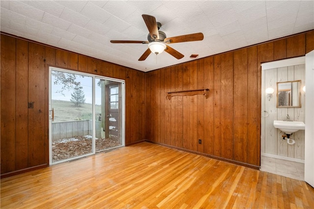 unfurnished room with ceiling fan, wood walls, a sink, wood finished floors, and baseboards