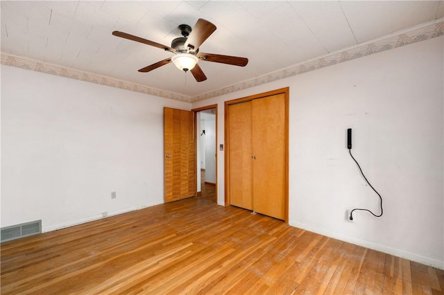 unfurnished bedroom featuring visible vents, baseboards, ornamental molding, a closet, and light wood finished floors