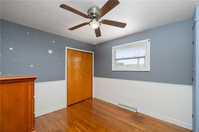 empty room featuring wainscoting, ceiling fan, visible vents, and hardwood / wood-style floors