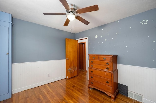 unfurnished bedroom with ceiling fan, wainscoting, wood-type flooring, and visible vents