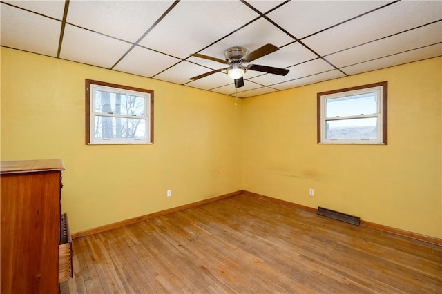 empty room with light wood finished floors, visible vents, baseboards, and a drop ceiling