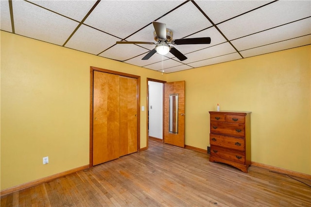 unfurnished bedroom with a paneled ceiling, ceiling fan, light wood-style flooring, and baseboards