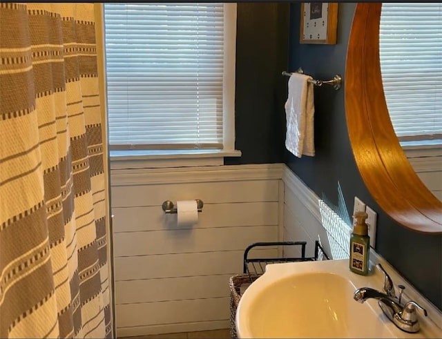 full bath with a wainscoted wall, curtained shower, a sink, and wood walls