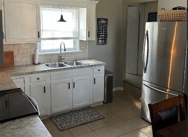 kitchen featuring freestanding refrigerator, white cabinets, a sink, and decorative backsplash