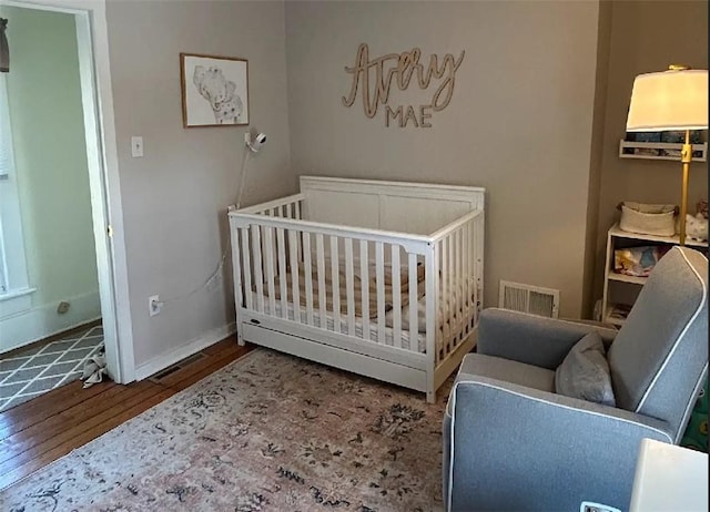 bedroom featuring baseboards, visible vents, a crib, and hardwood / wood-style floors