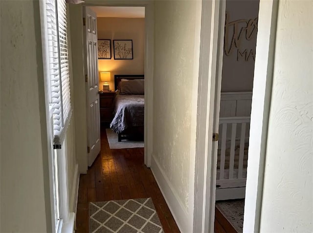 hall featuring a textured wall, baseboards, and wood finished floors