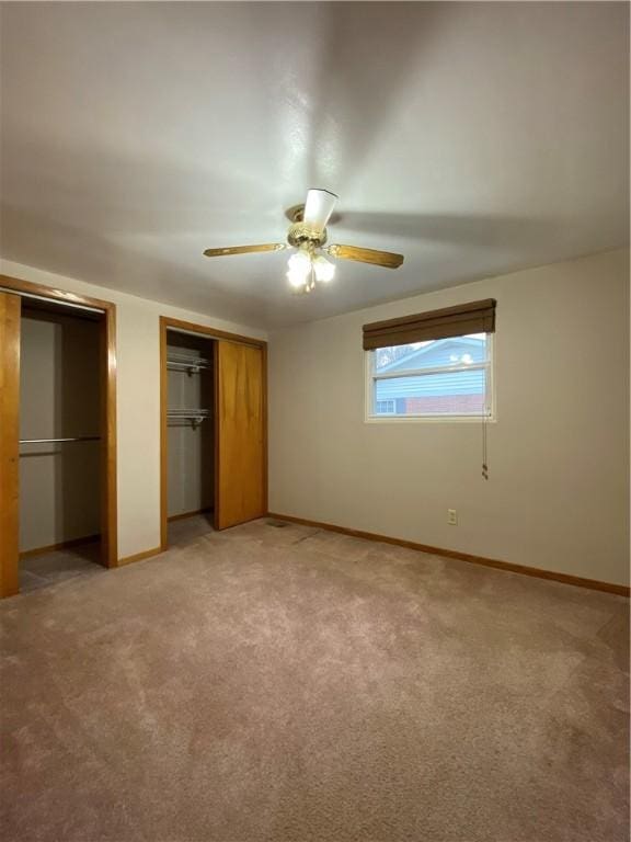 unfurnished bedroom featuring baseboards, two closets, and light colored carpet