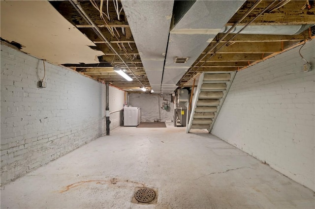 unfinished below grade area with washer / clothes dryer, visible vents, brick wall, and heating unit