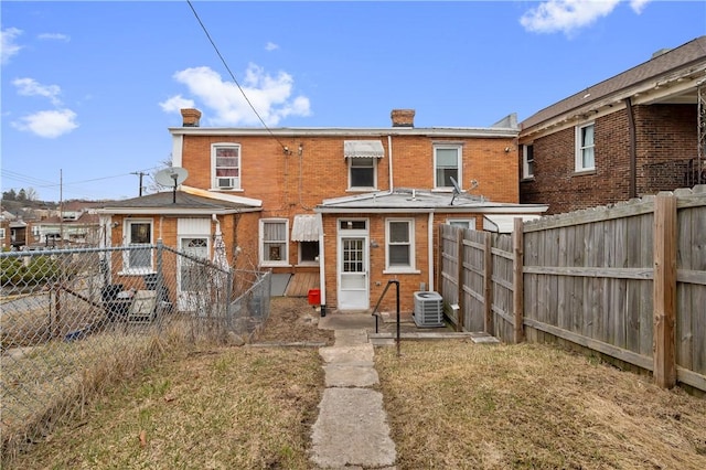 rear view of house with brick siding, a chimney, central AC unit, and a fenced backyard