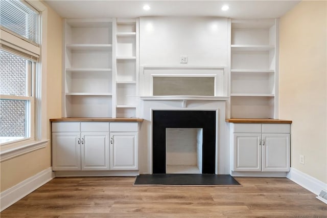 unfurnished living room with light wood finished floors, a fireplace with flush hearth, visible vents, and baseboards