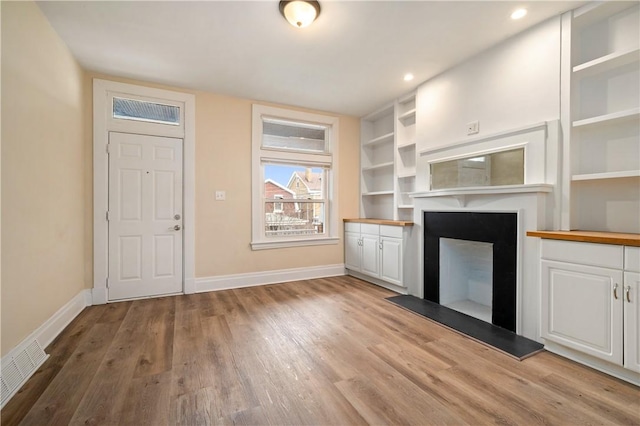 unfurnished living room with visible vents, a fireplace, light wood-style flooring, and baseboards