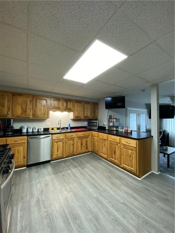 kitchen featuring brown cabinets, stainless steel appliances, dark countertops, a sink, and light wood-type flooring