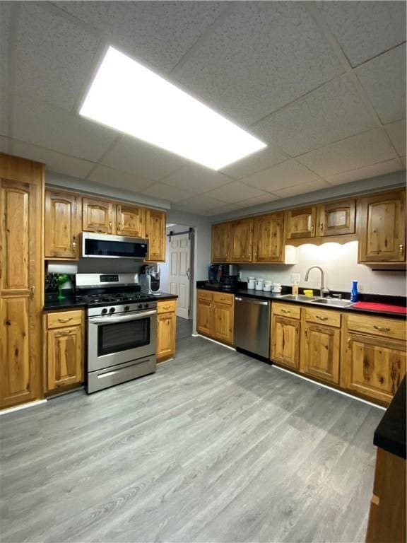 kitchen with appliances with stainless steel finishes, dark countertops, light wood-type flooring, and brown cabinetry