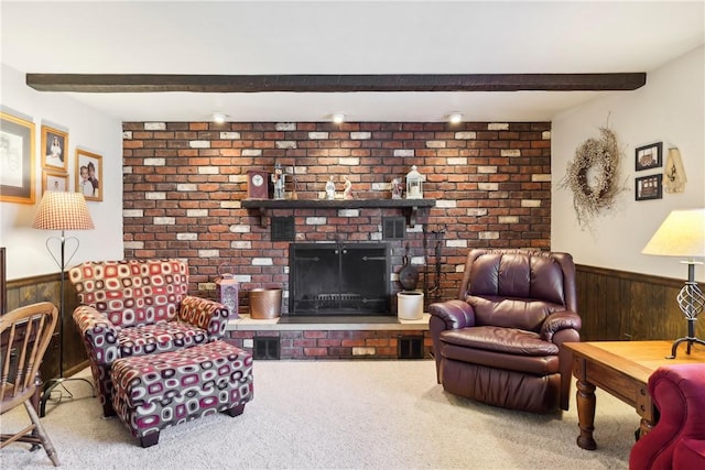 carpeted living area with a wainscoted wall, wood walls, beamed ceiling, and a brick fireplace