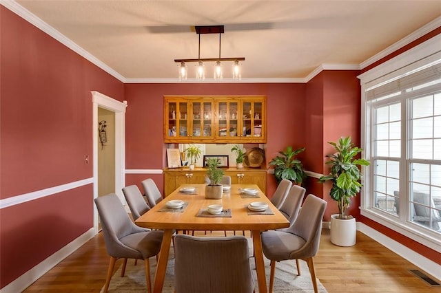 dining area with light wood-style floors, a wealth of natural light, visible vents, and crown molding