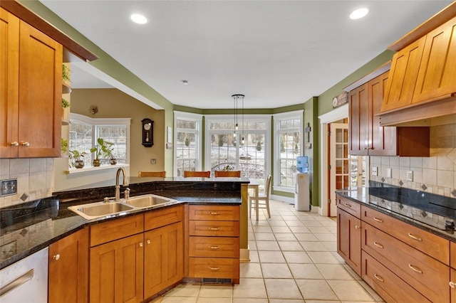 kitchen with light tile patterned floors, dishwasher, dark stone countertops, a peninsula, and a sink