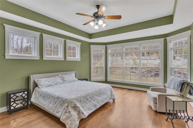 bedroom featuring a raised ceiling, multiple windows, and wood finished floors