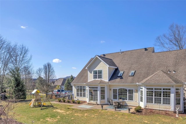 back of house with a yard, roof with shingles, a playground, and a patio