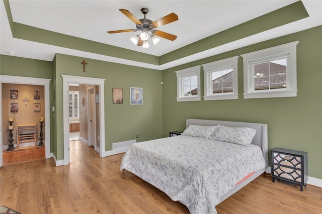 bedroom featuring a tray ceiling, visible vents, and wood finished floors