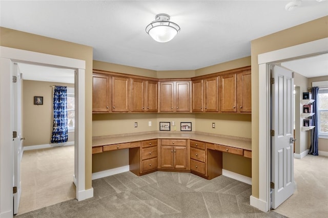 interior space featuring light colored carpet, built in desk, and baseboards