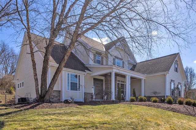 view of front facade featuring a shingled roof, a front yard, stone siding, and covered porch