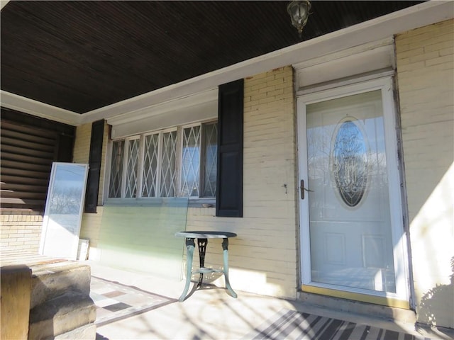 doorway to property with covered porch and brick siding