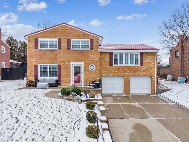 split level home featuring driveway, metal roof, an attached garage, fence, and brick siding