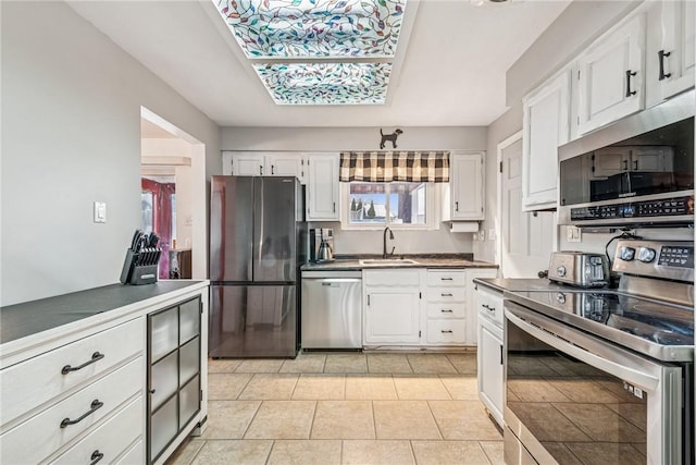 kitchen featuring light tile patterned floors, stainless steel appliances, a sink, white cabinets, and dark countertops