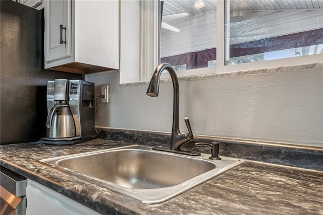 room details featuring a textured wall, dark countertops, a sink, and white cabinetry