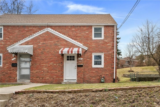 townhome / multi-family property with roof with shingles, brick siding, and a front lawn