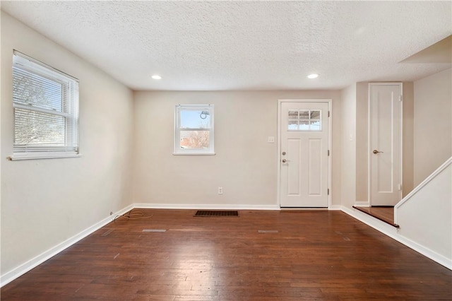 foyer entrance featuring a textured ceiling, wood-type flooring, visible vents, and baseboards