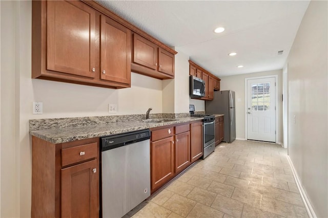 kitchen featuring baseboards, appliances with stainless steel finishes, brown cabinets, light stone countertops, and a sink