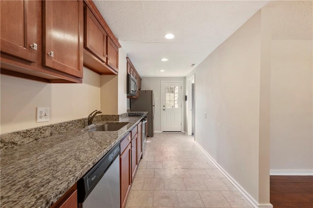 kitchen featuring baseboards, appliances with stainless steel finishes, brown cabinets, stone counters, and a sink