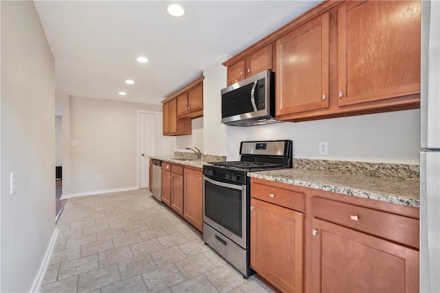 kitchen with stainless steel appliances, recessed lighting, brown cabinetry, a sink, and baseboards