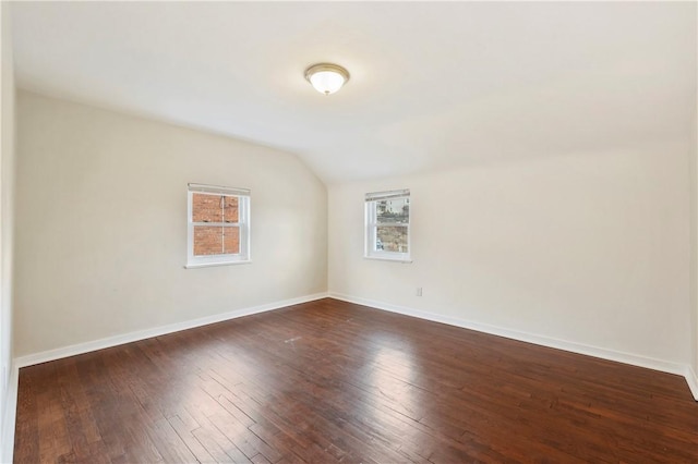 spare room with dark wood-style floors, vaulted ceiling, and baseboards