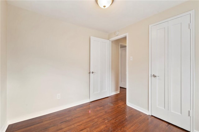 unfurnished bedroom featuring dark wood-type flooring, a closet, and baseboards