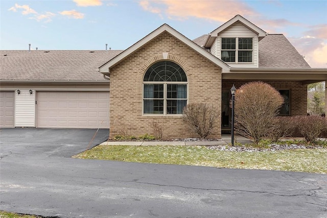 view of front of property with an attached garage, roof with shingles, aphalt driveway, and brick siding